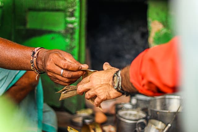 Hands passing a paper-wrapped bundle of vegetables across a wooden counter