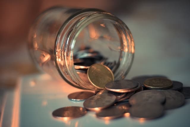 A glass jar marked with chalk, a single coin caught mid-fall